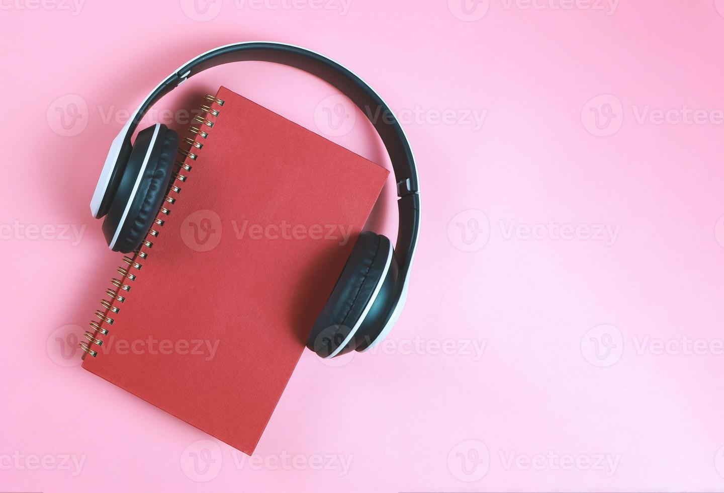 flat lay of red notebook or  diary or planner covered with headphones on pink background with copy space.  Audio book or podcast concept. photo
