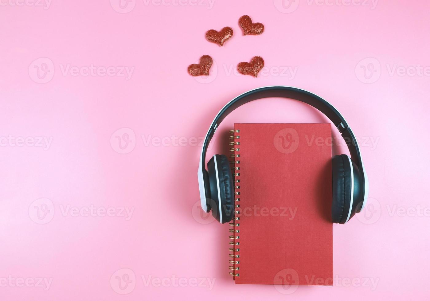 flat lay of red notebook covered with headphones on pink  background decorated with red glitter hearts , copy space. Audio book, podcast, .love diary, valentine's day. photo