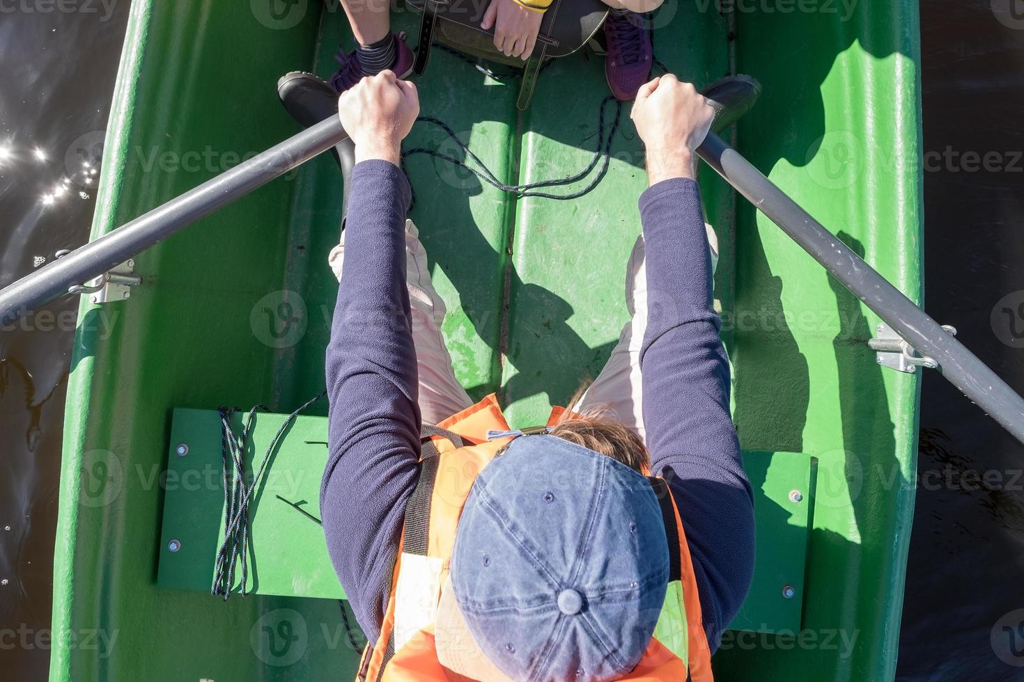 Man in a life jacket rowing with oars on a boat and across the lake. Active lifestyle concept. Top view. photo