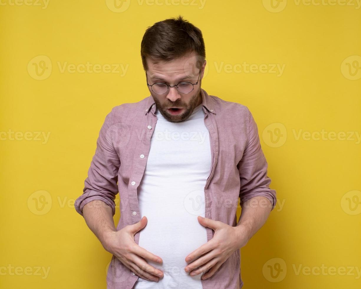 Man is shocked by his overweight, he looks at the excess fat on stomach and holds it with hands. Healthy lifestyle concept. photo