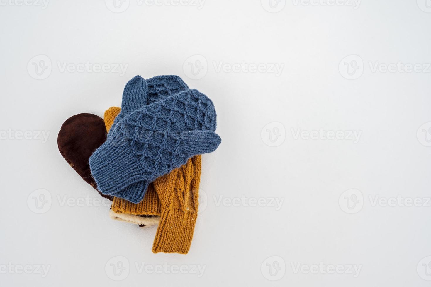 Several pairs of knitted, warm mittens lie in a pile on white, clean snow, on a cloudy winter day. Copy space. photo