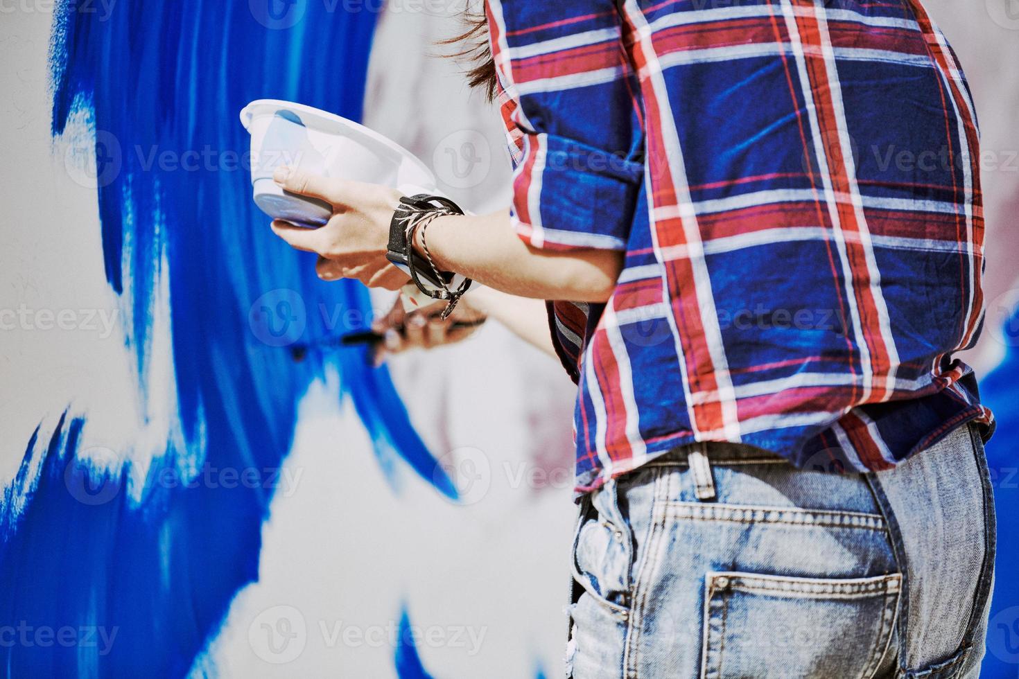 Female artist working on abstract acrylic painting, hand holding paint brush, large canvas outdoor photo