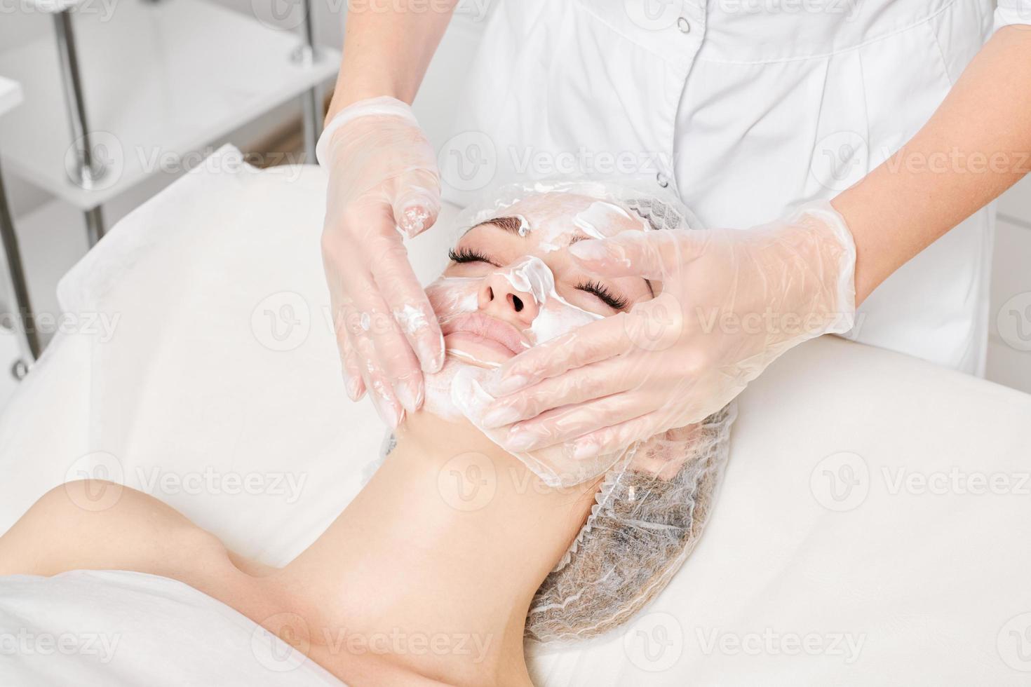 Cosmetologist massages cream mask into woman face skin for rejuvenation, procedure in beauty salon photo