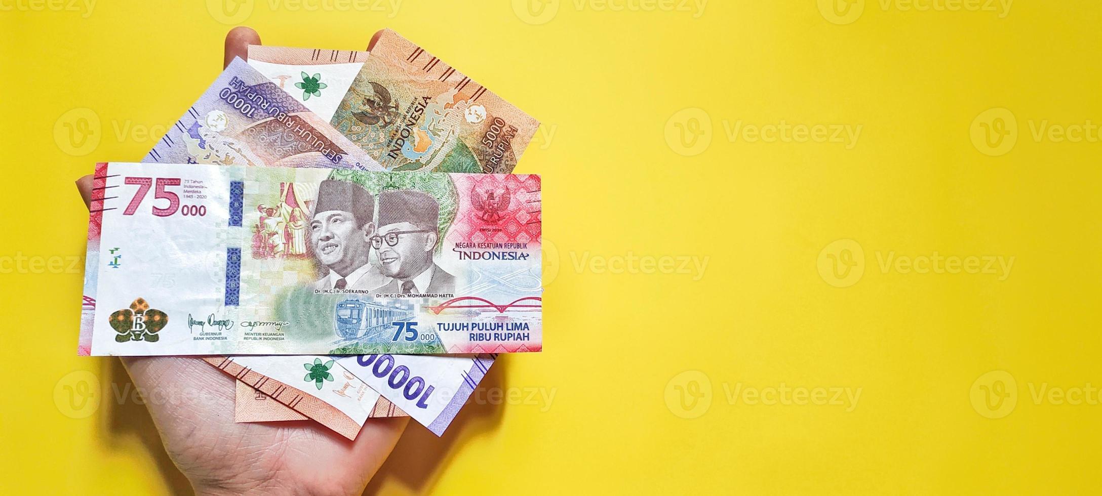 hombre que sostiene billetes en rupias indonesias la última edición, aislado en un fondo amarillo. foto