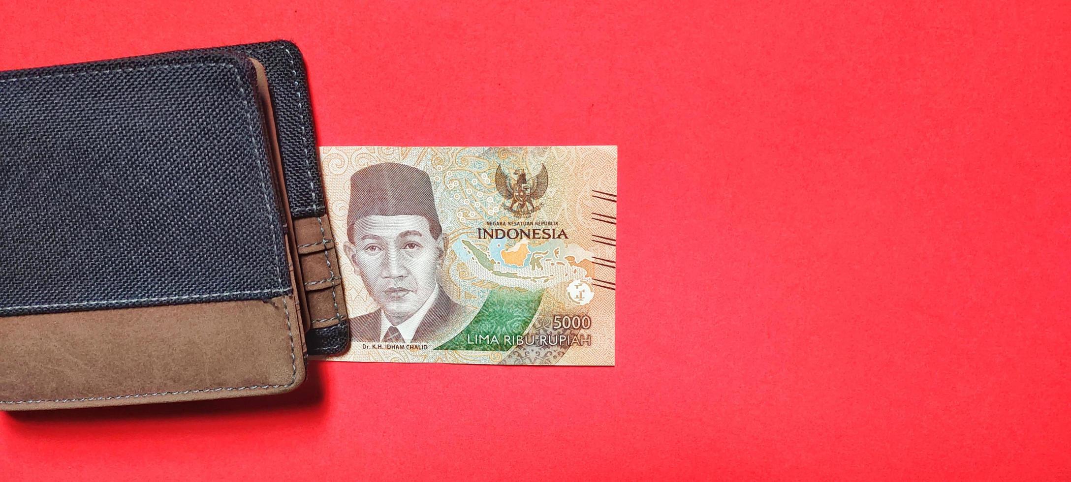 la última edición de billetes de rupias indonesias por valor de 5.000 rupias y una cartera marrón. foto