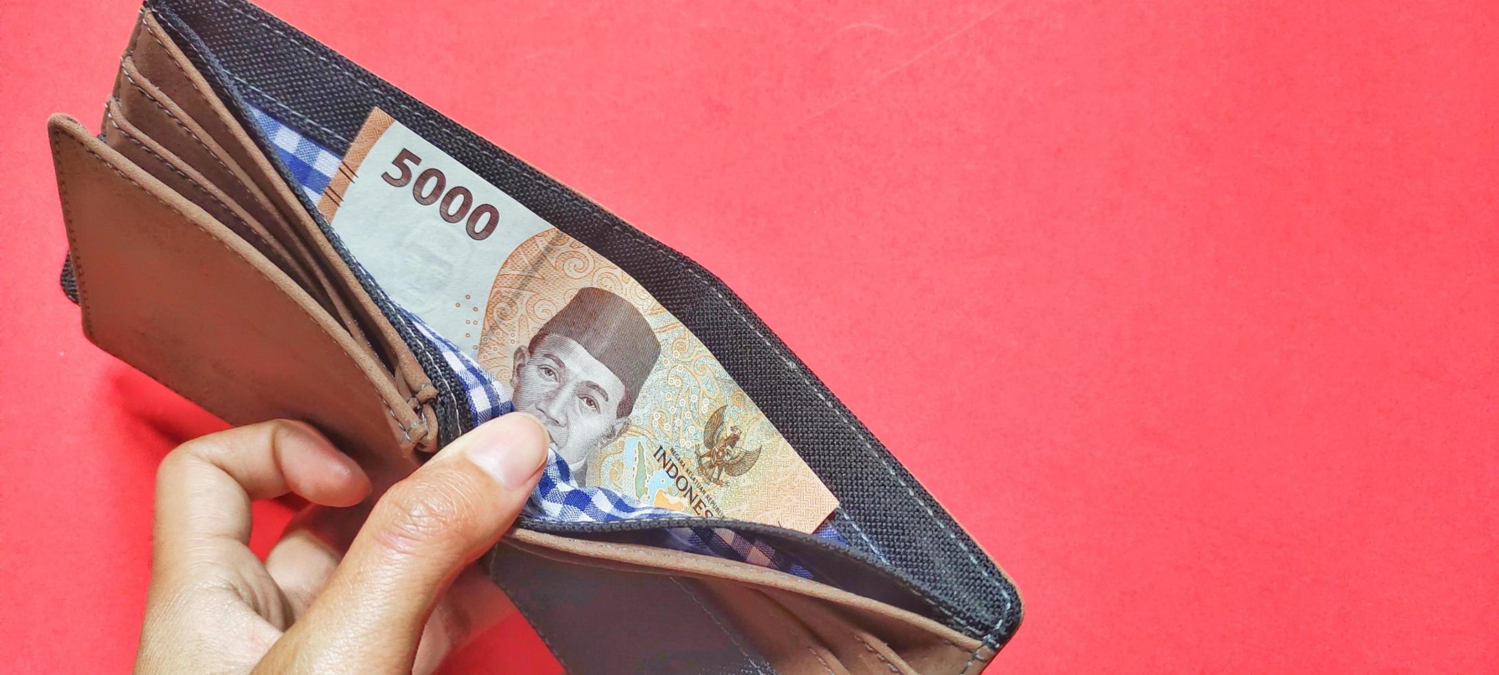 Man holding a wallet containing the latest edition of Indonesian banknotes. photo
