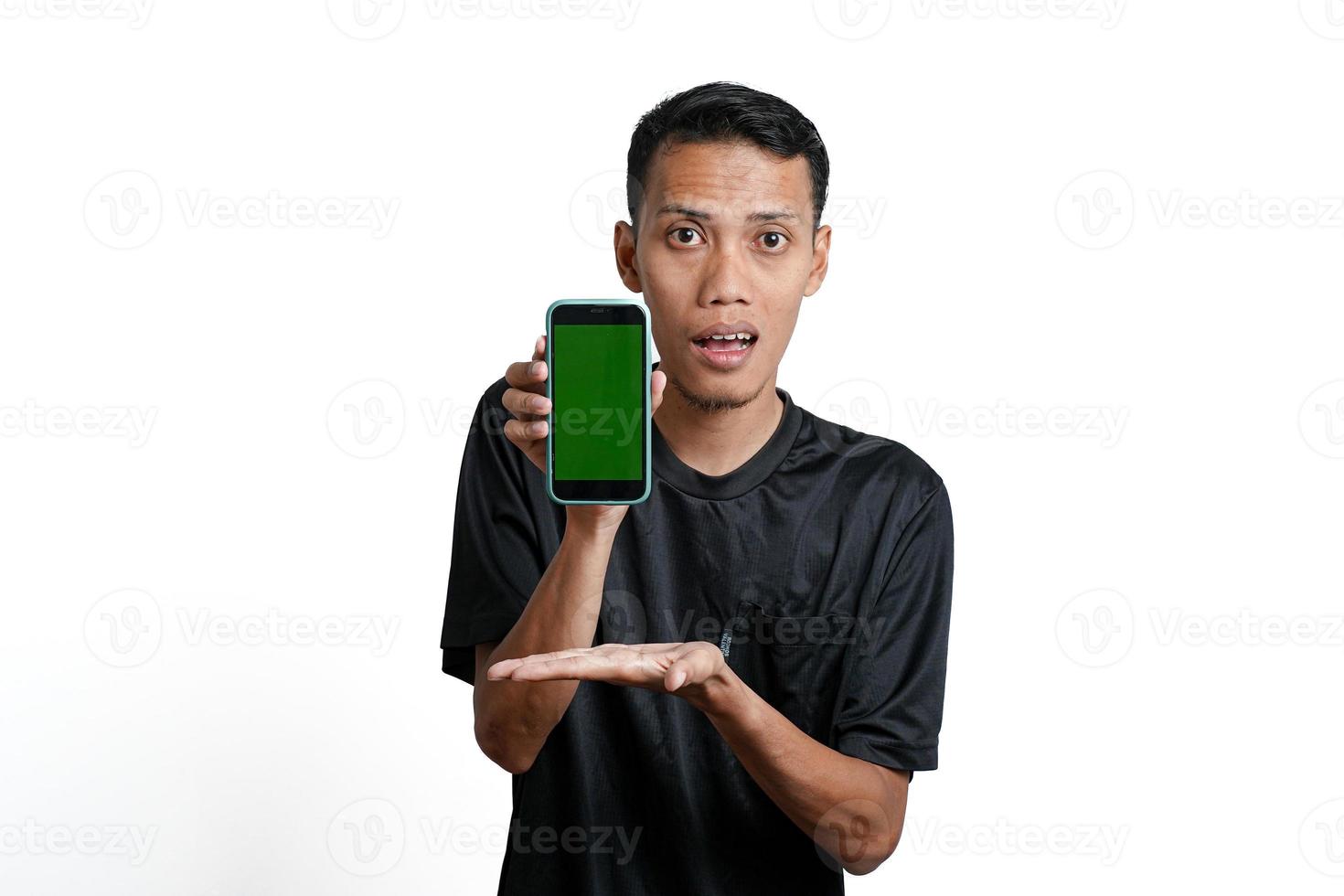 excited asian man wearing black workout t-shirt, pointing at green screen of smartphone. Isolated by white background photo