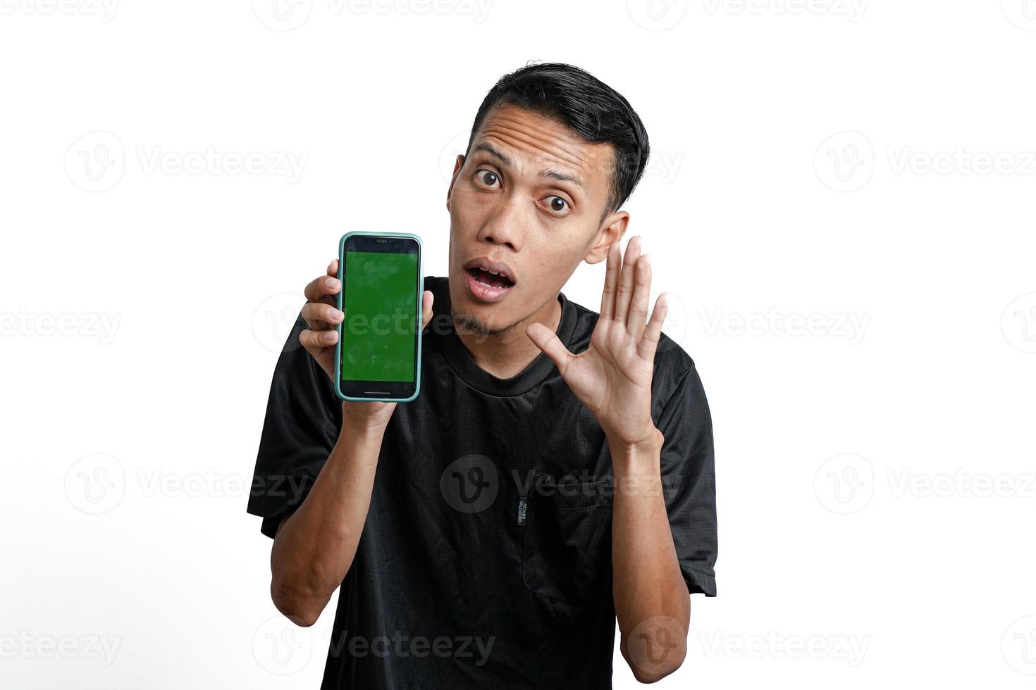 excited asian man wearing black workout t-shirt, pointing at green screen of smartphone. Isolated by white background photo