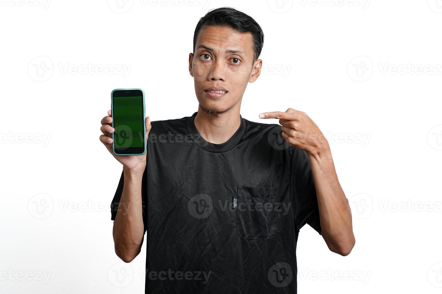 excited asian man wearing black workout t-shirt, pointing at green screen of smartphone. Isolated by white background photo