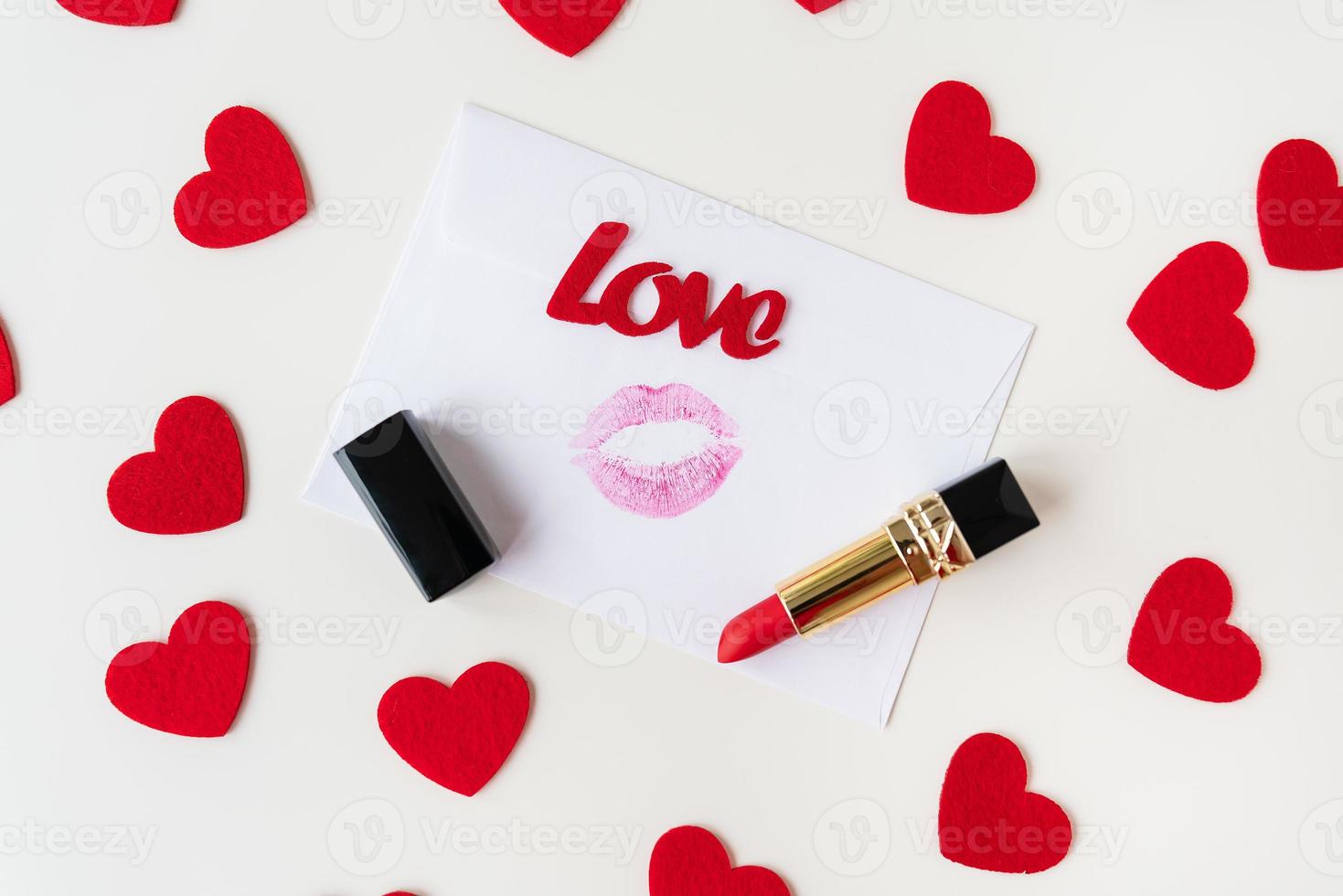 A white envelope with a lip print of red lipstick on a background of small red hearts. February 14 Valentine's Day concept. photo