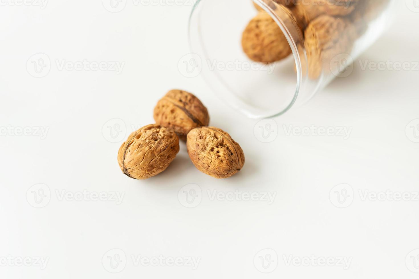 Beautiful whole walnut kernels in a glass jar, whole nuts in shell spilling on the table. Selective focus, noise. photo