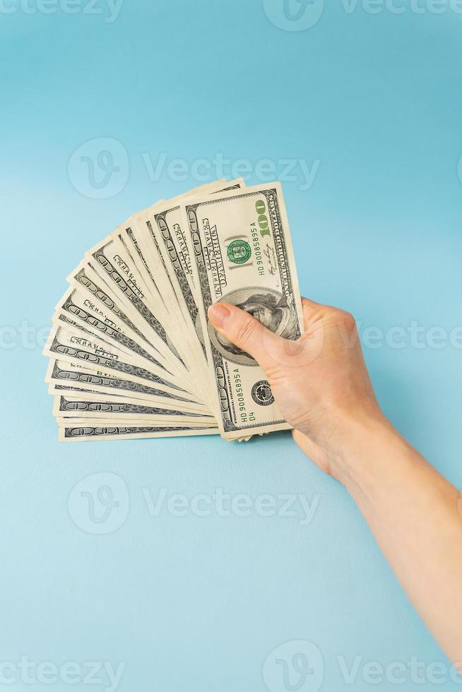 manos femeninas sosteniendo billetes de 100 dólares aislados en fondo azul. foto