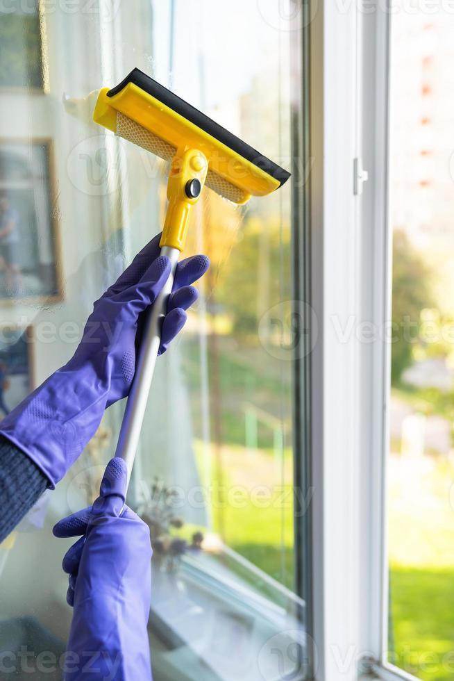 concepto de limpieza y limpieza de la casa. una joven con guantes morados y un trapeador amarillo en las manos lava la ventana. foto