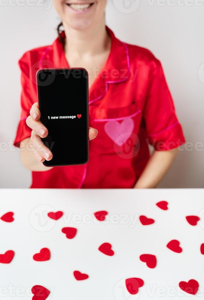 A happy girl is holding a smartphone with an activated screen with 1 SMS message in the shape of a heart. Concept of Valentine's Day, February 14. photo