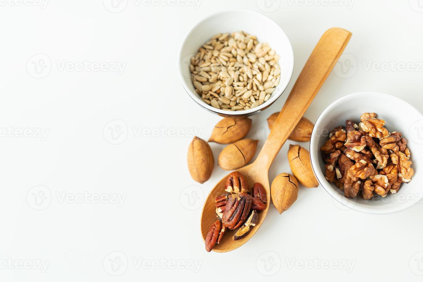 A close-up of a plate with different nuts and seeds along with a wooden spoon lie on a white table. The concept of weight loss, healthy eating, overweight. Fitness menu. photo