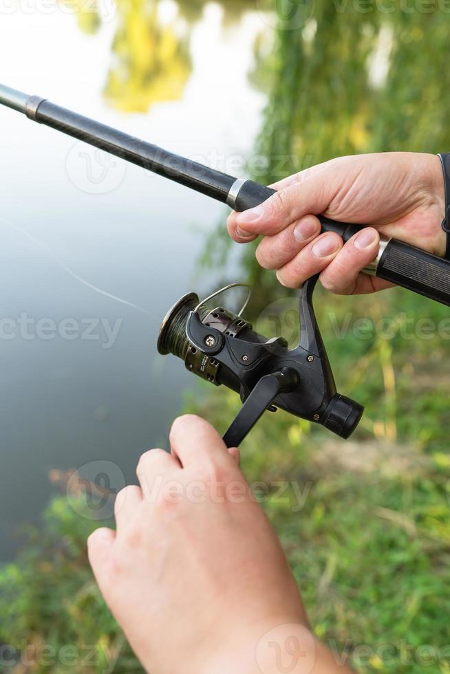 Fishing Reel. The guy spins the coil on the background of the lake. The concept of relaxation and hobby for the soul. photo