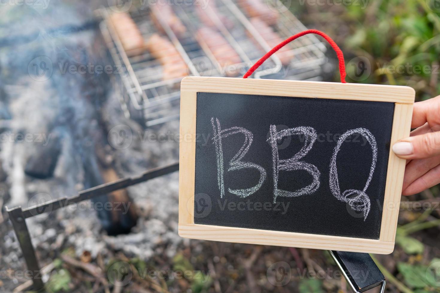 la inscripción barbacoa en un plato negro, un fuego contra el fondo de una parrilla en la que se encuentran las salchichas. foto