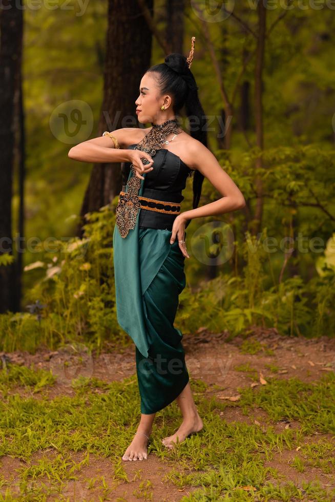 Beautiful Indonesian dancers with traditional green costumes and black tied hair posing inside the forest photo