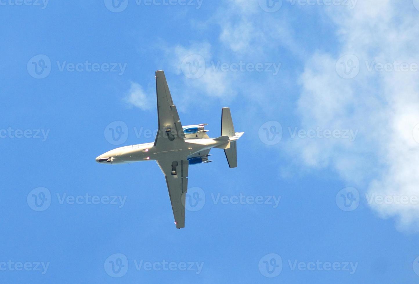 A twin engine business jet with its landing gear down and landing lights on against a sky with light clouds. photo