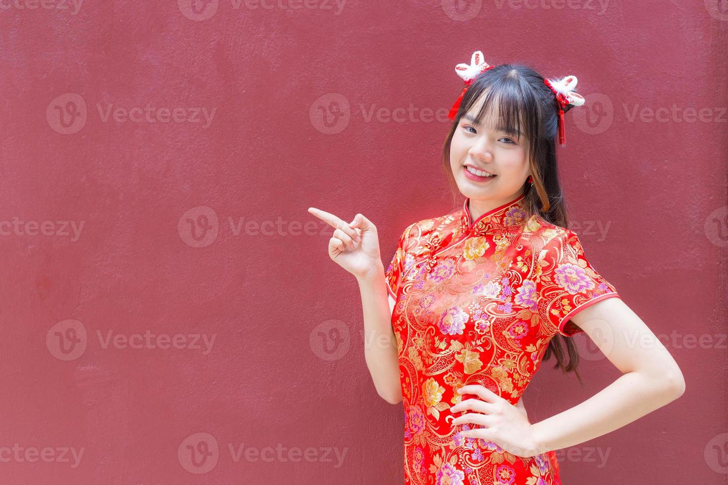 Cute Asian girl with long hair who wears a red Cheongsam dress in Chinese new year theme while she shows her hand to present something on a red background. photo