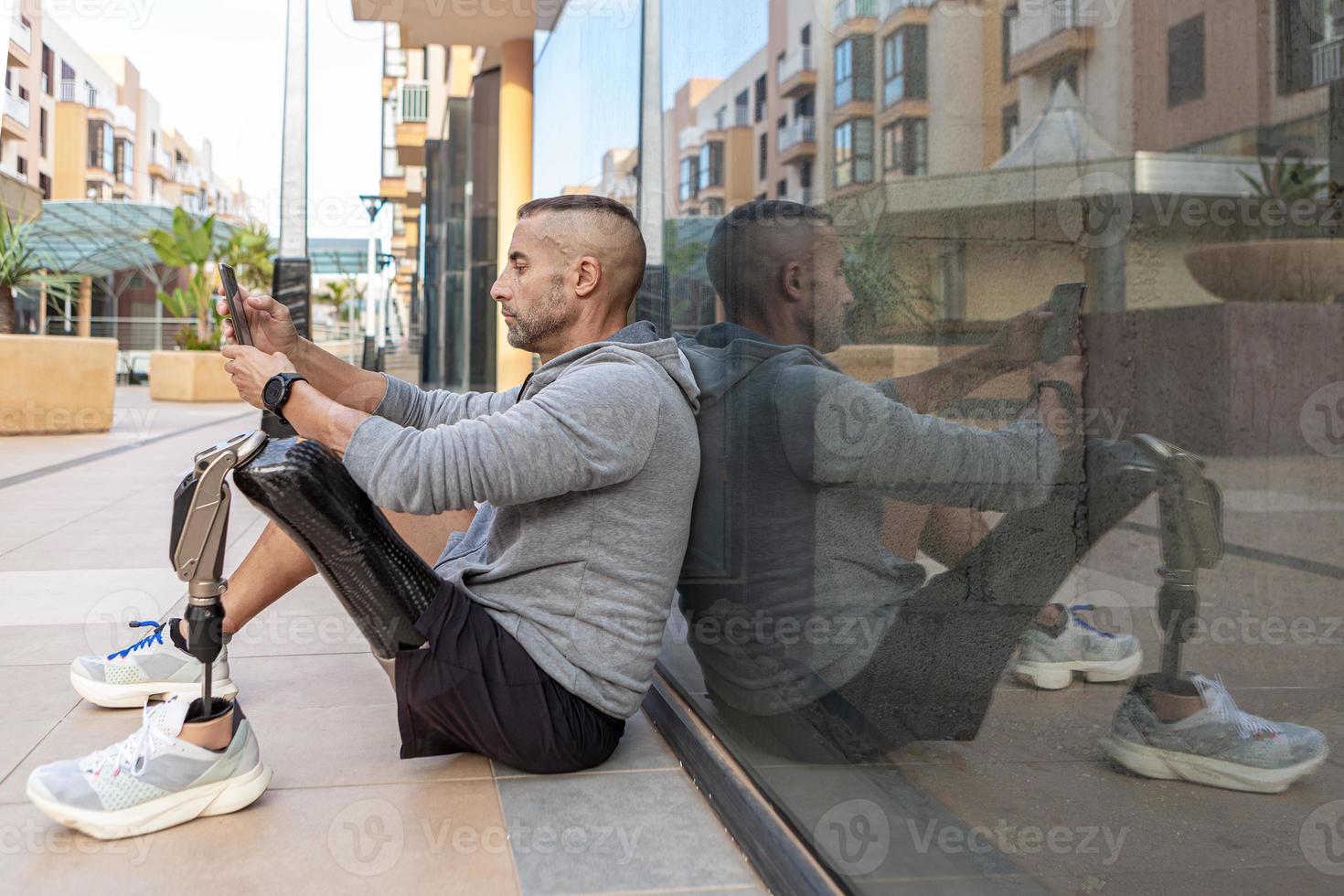 hombre amputado usando un teléfono inteligente cerca de una pared de vidrio foto