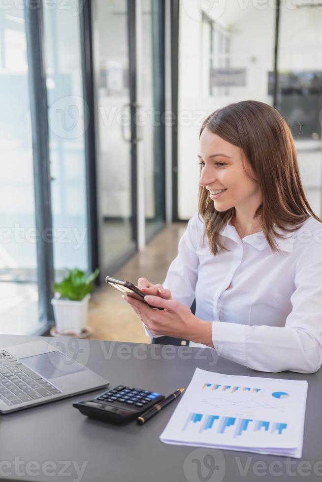 marketing, finance, accounting, planning, White biracial businesswoman using mobile phone to contact clients informing them of company business partnerships on office table with laptop and documents. photo