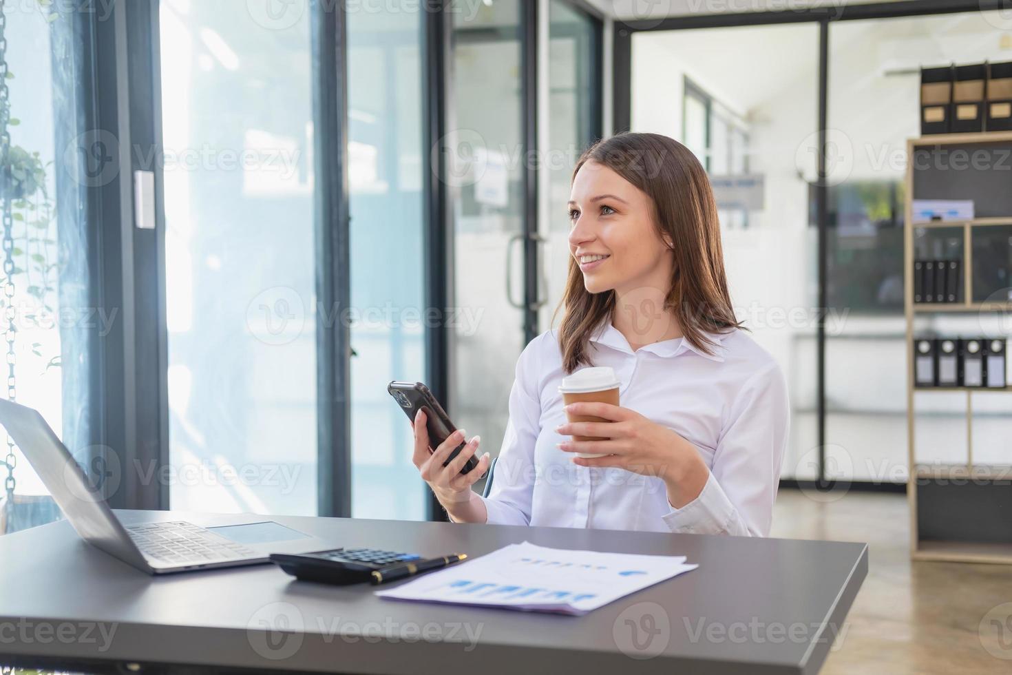 marketing, finance, accounting, planning, White biracial businesswoman using mobile phone to contact clients informing them of company business partnerships on office table with laptop and documents. photo