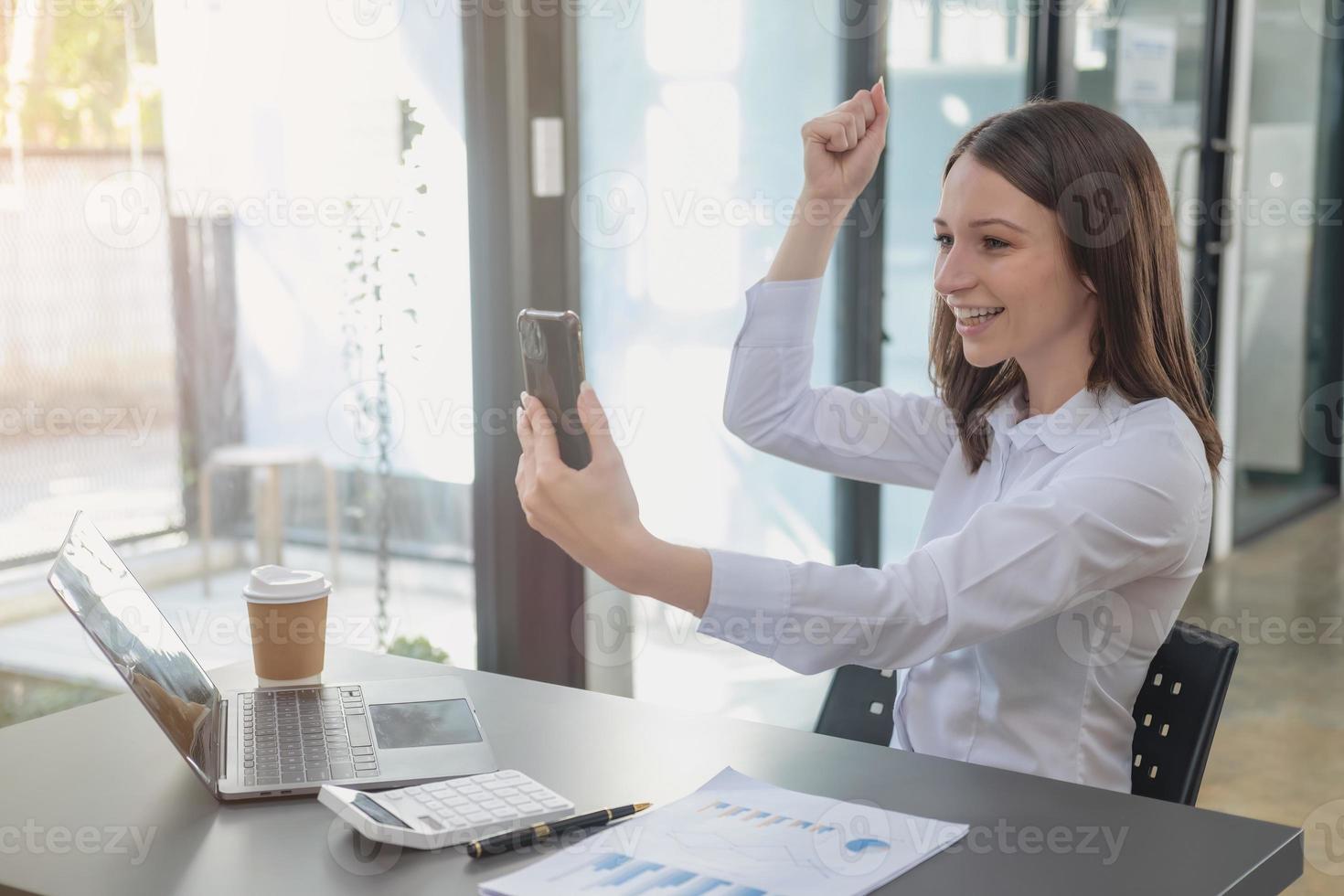 marketing, finanzas, contabilidad, planificación. mujer de negocios caucásica que sostiene un teléfono móvil y muestra buena voluntad en el cliente que se une al negocio con la empresa para aumentar las ganancias de la oficina y los documentos de la computadora portátil foto