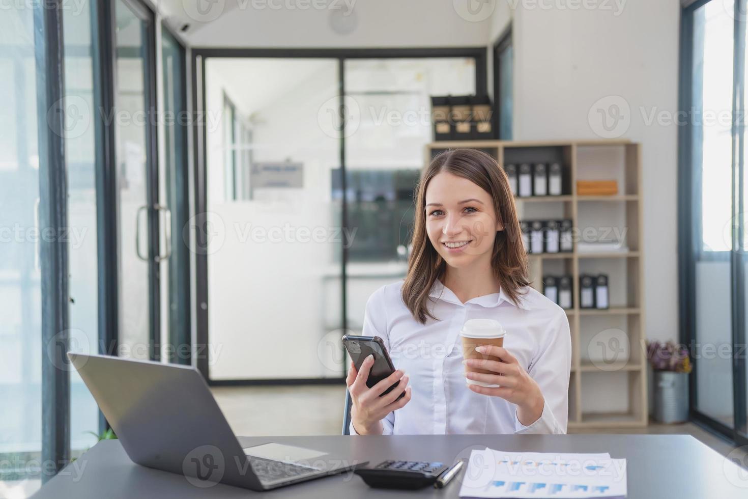 marketing, finance, accounting, planning, White biracial businesswoman using mobile phone to contact clients informing them of company business partnerships on office table with laptop and documents. photo