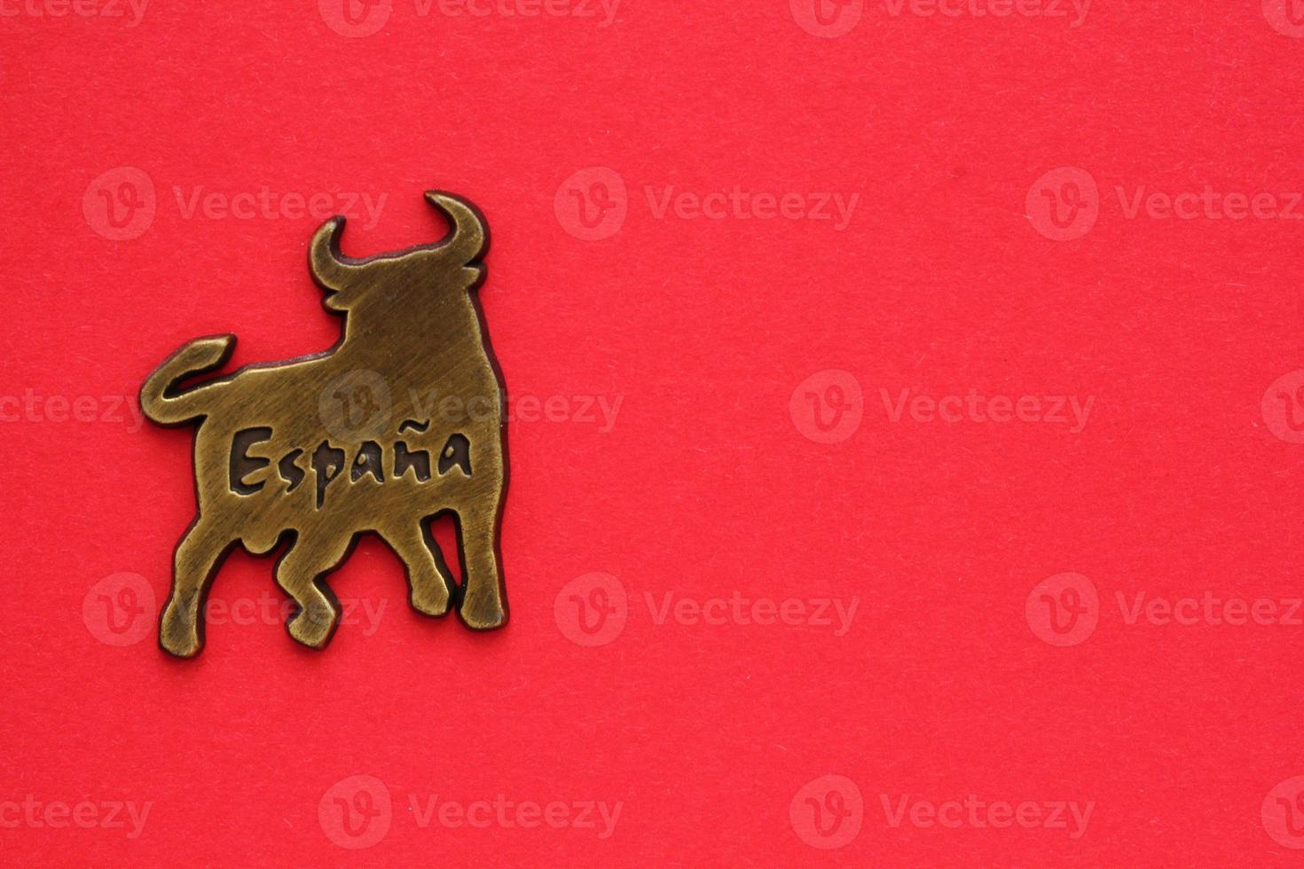 Metal souvenir fridge magnet of bull Spain isolated on red background. Travel memory concept. Gift typical product for tourists from trip. Home decor. Top view, flat lay, close up. Copy space for text photo