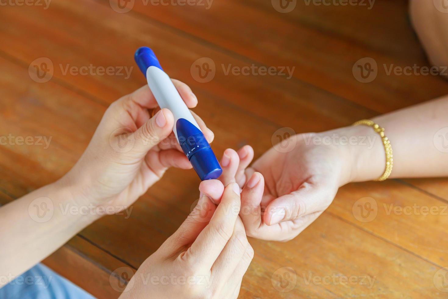 Close up of two woman using lancet on finger to check blood sugar level by Glucose meter using as Medicine, diabetes, glycemia, health care and people concept. photo