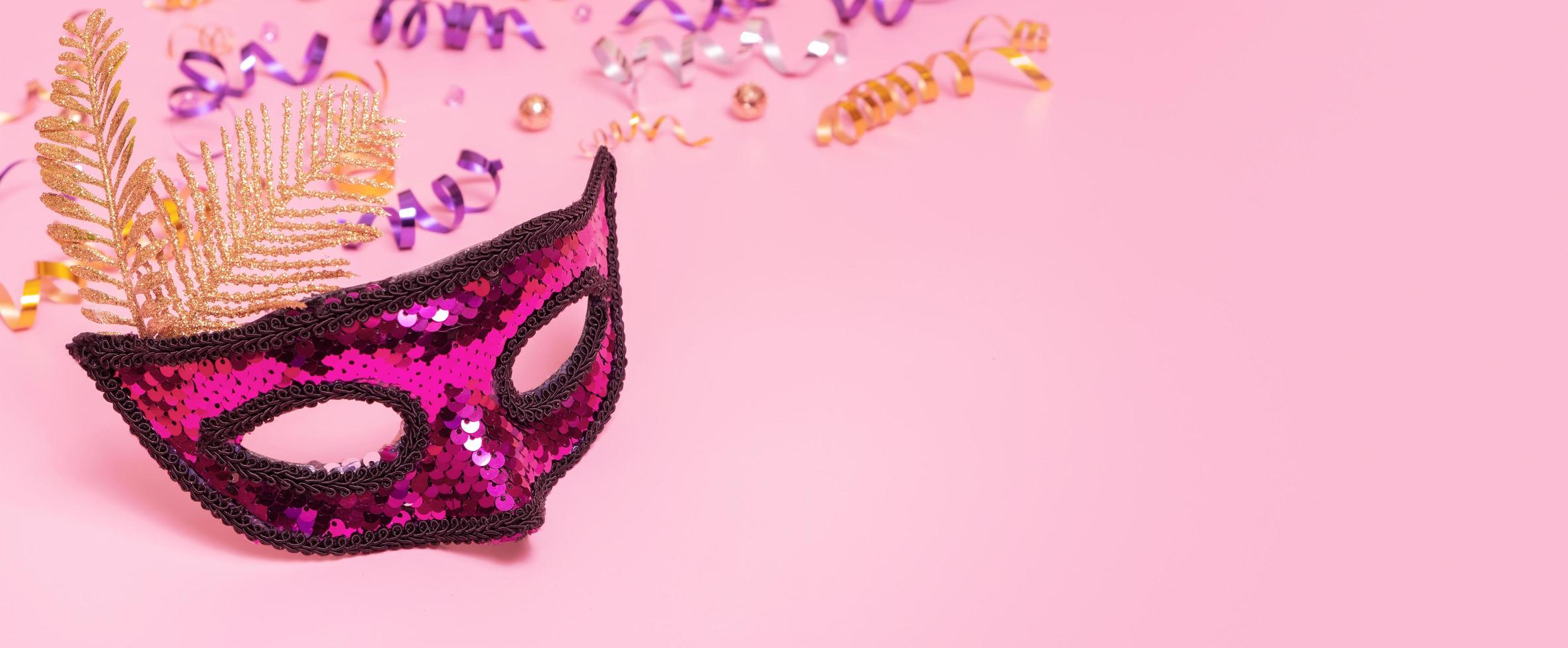 Festive face mask for masquerade or carnival celebration on colored background with tinsel. Banner format photo