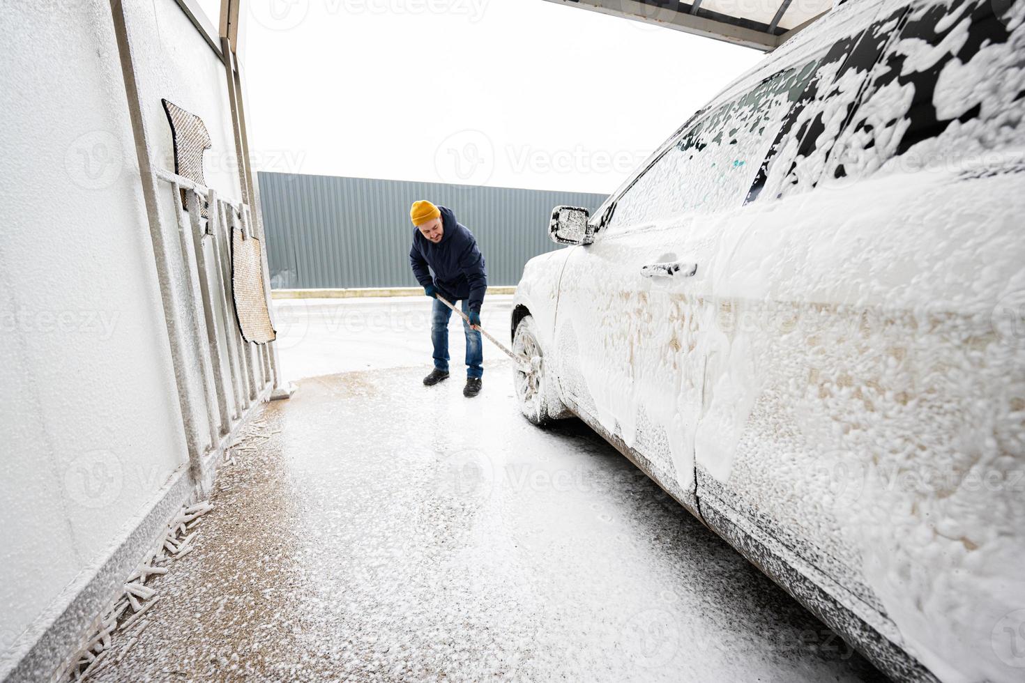 Man washing american SUV car with mop at a self service wash in cold weather. photo