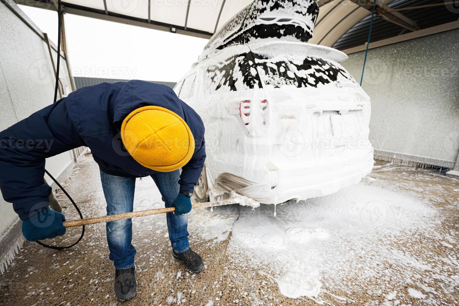 Man washing american SUV car with mop at a self service wash in cold weather. photo