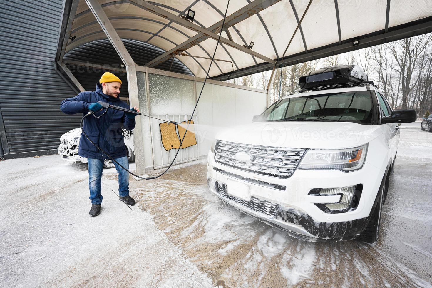 Man washing high pressure water american SUV car with roof rack at self service wash in cold weather. photo