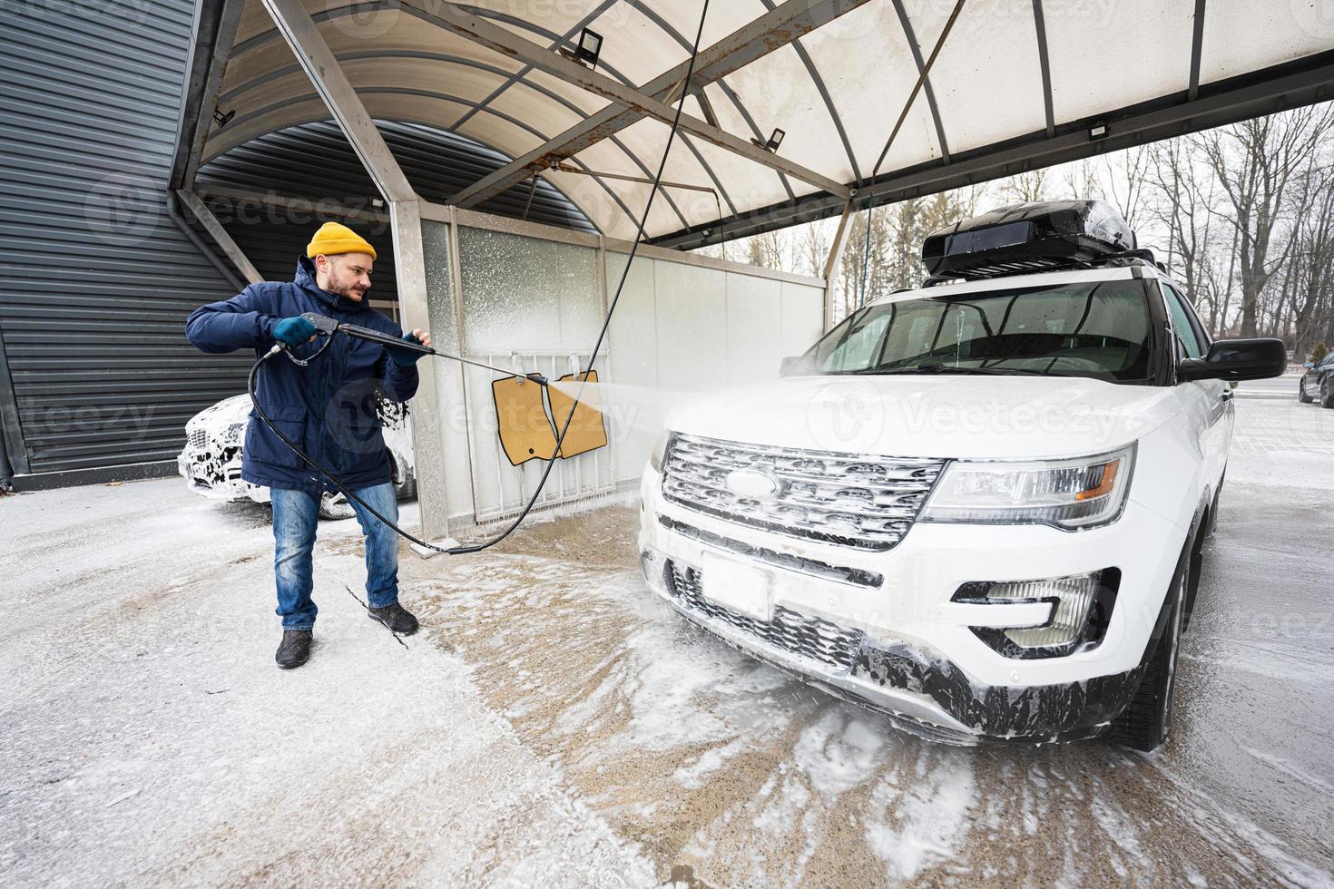 hombre lavando agua a alta presión coche suv americano con portaequipajes en autoservicio de lavado en clima frío. foto