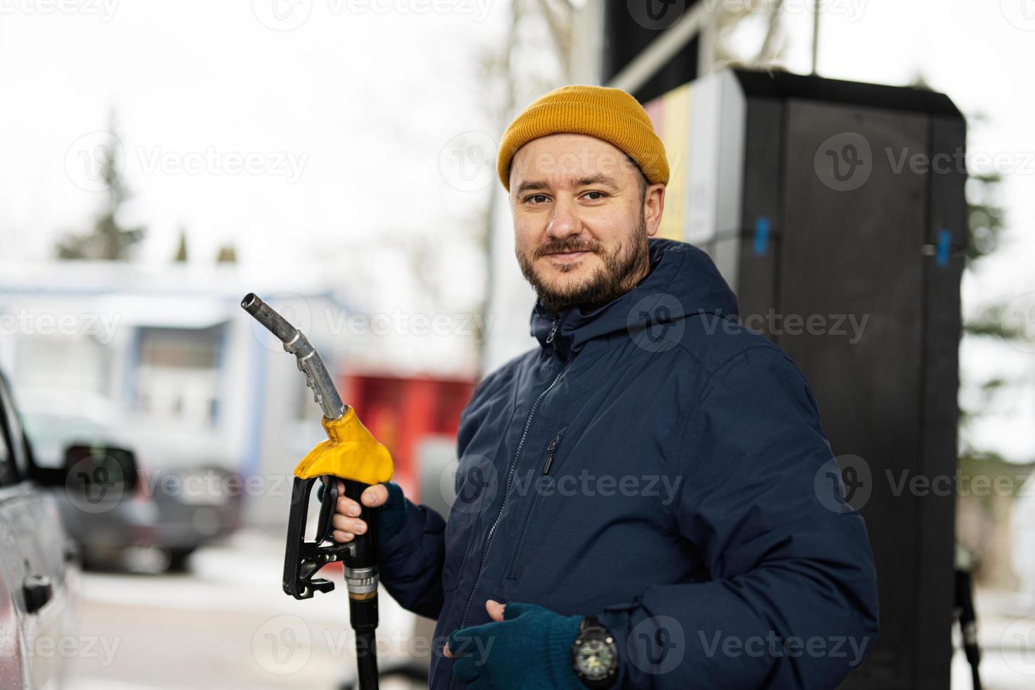 el hombre sostiene la bomba de combustible mientras reabastece su camión en la gasolinera cuando hace frío. foto