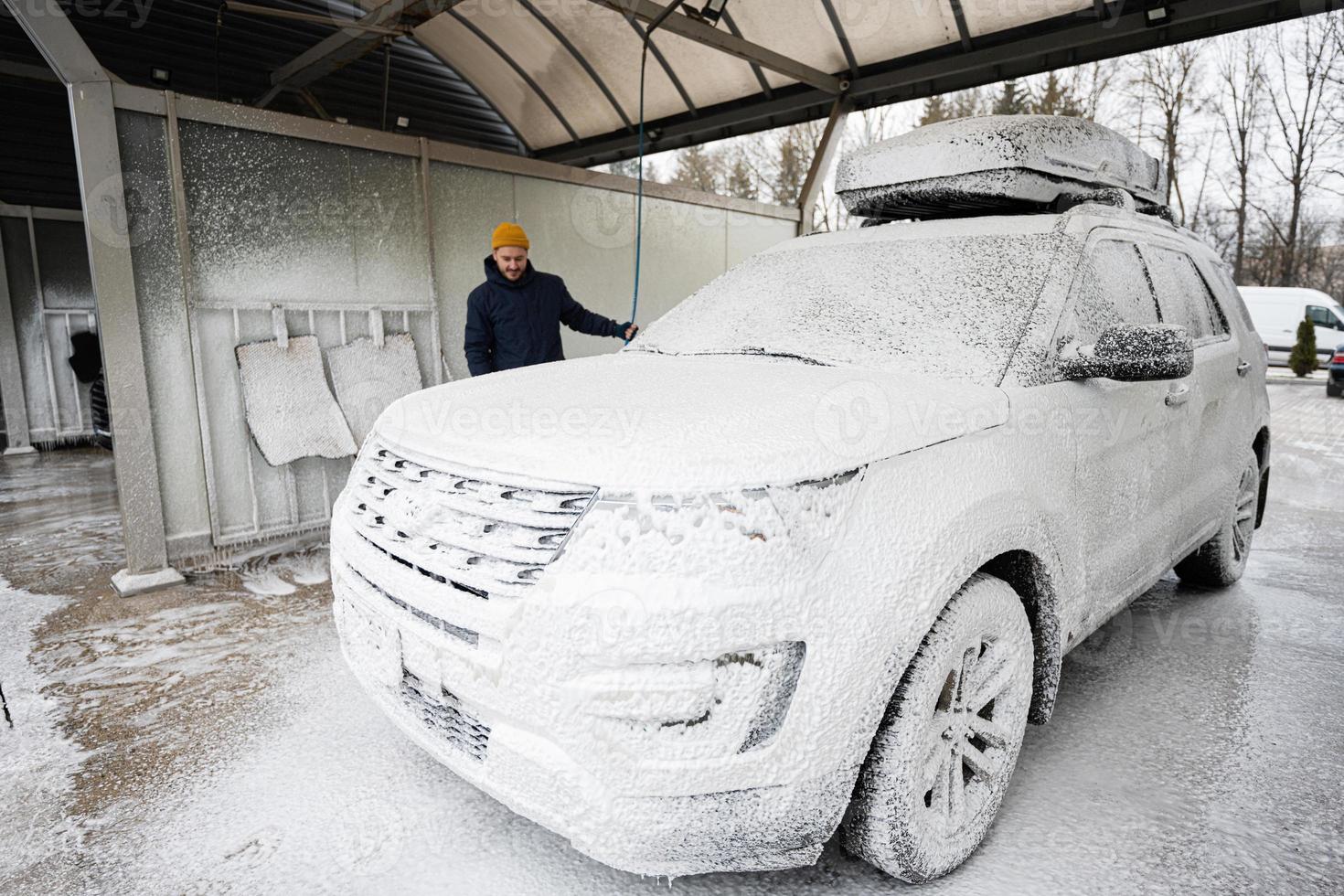 hombre lavando un automóvil suv americano con portaequipajes en un lavado de autoservicio en clima frío. foto