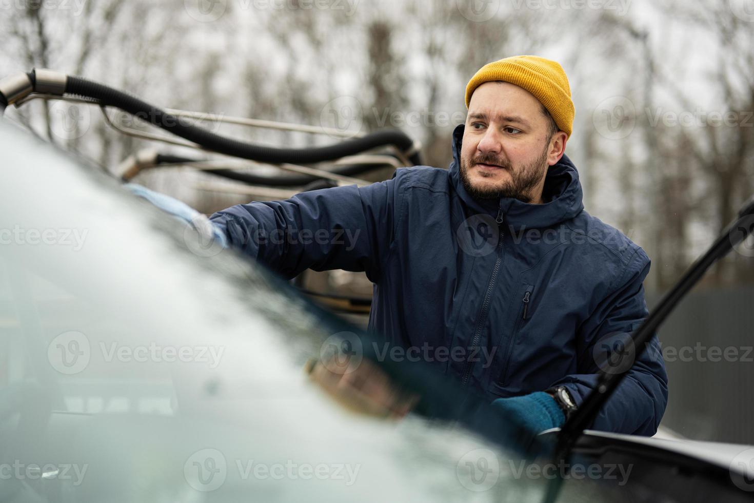 Man wipes american SUV car windshield with a microfiber cloth after washing in cold weather. photo