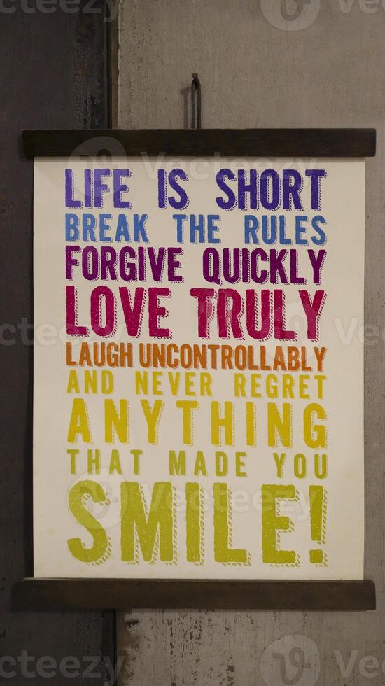 Hanging motivational word sign at the wall about life that say life is short brake the rules forgive quickly love truly laugh uncontrollably and never regret anything that made you smile. photo