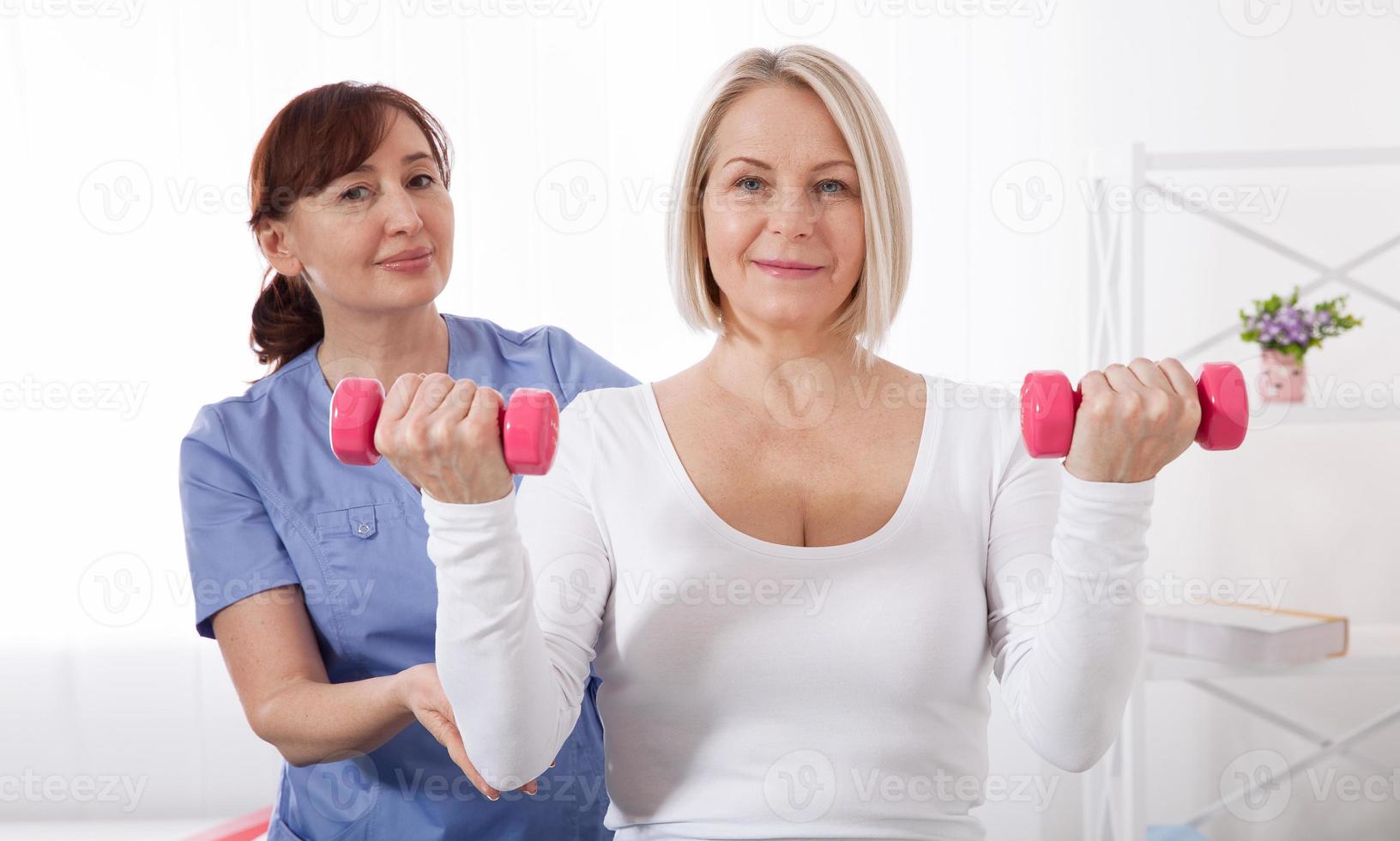 A physiotherapist helps an older woman recover from an injury through exercise with dumbbells. photo