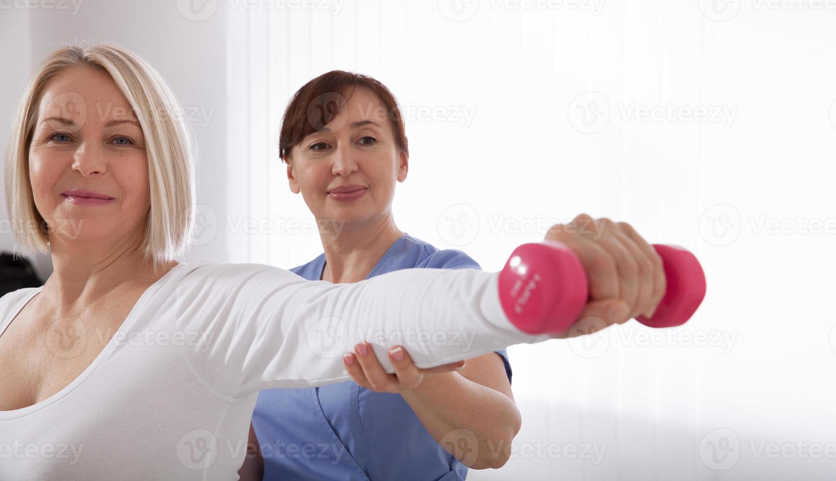 Modern rehabilitation physiotherapy. Physiotherapist helps an middle aged woman recover from an injury through exercise with dumbbells. photo