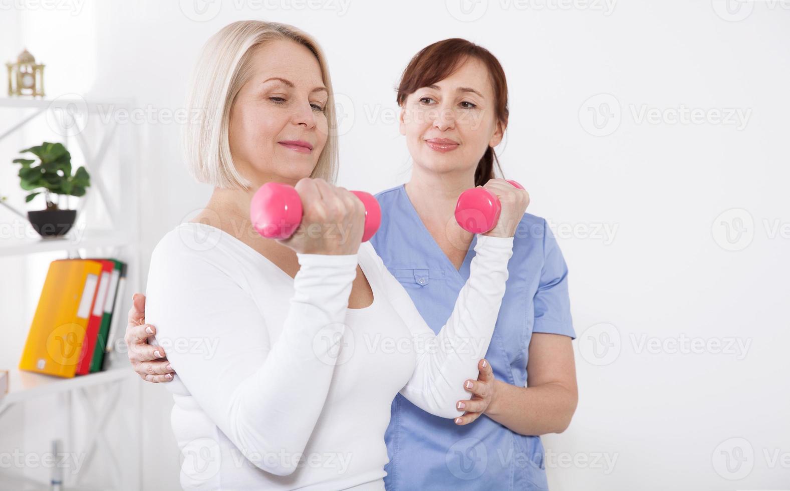 A physiotherapist helps an older woman recover from an injury through exercise with dumbbells. photo