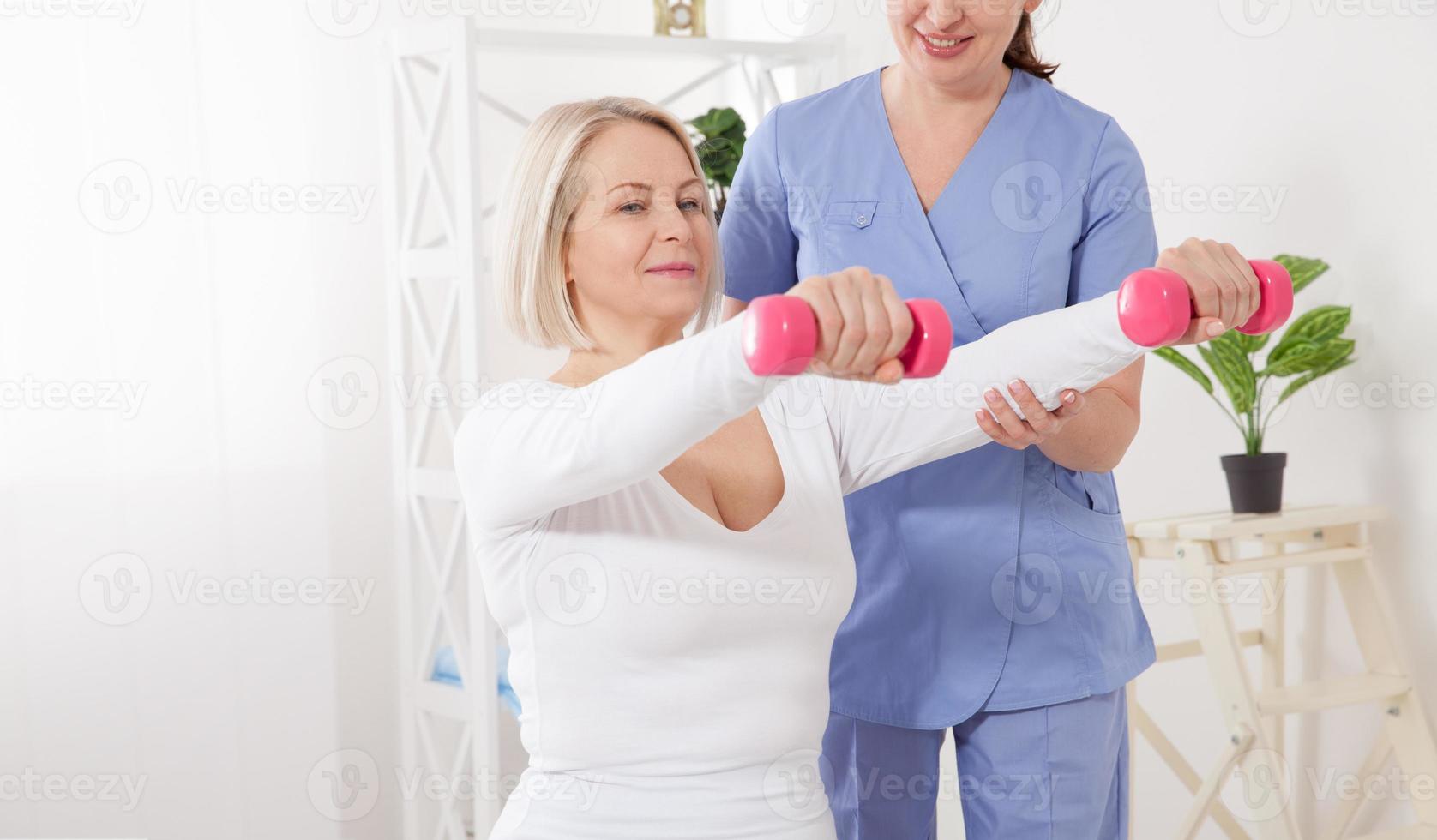 fisioterapia de rehabilitación moderna. fisioterapeuta ayuda a una mujer de mediana edad a recuperarse de una lesión mediante el ejercicio con pesas. foto