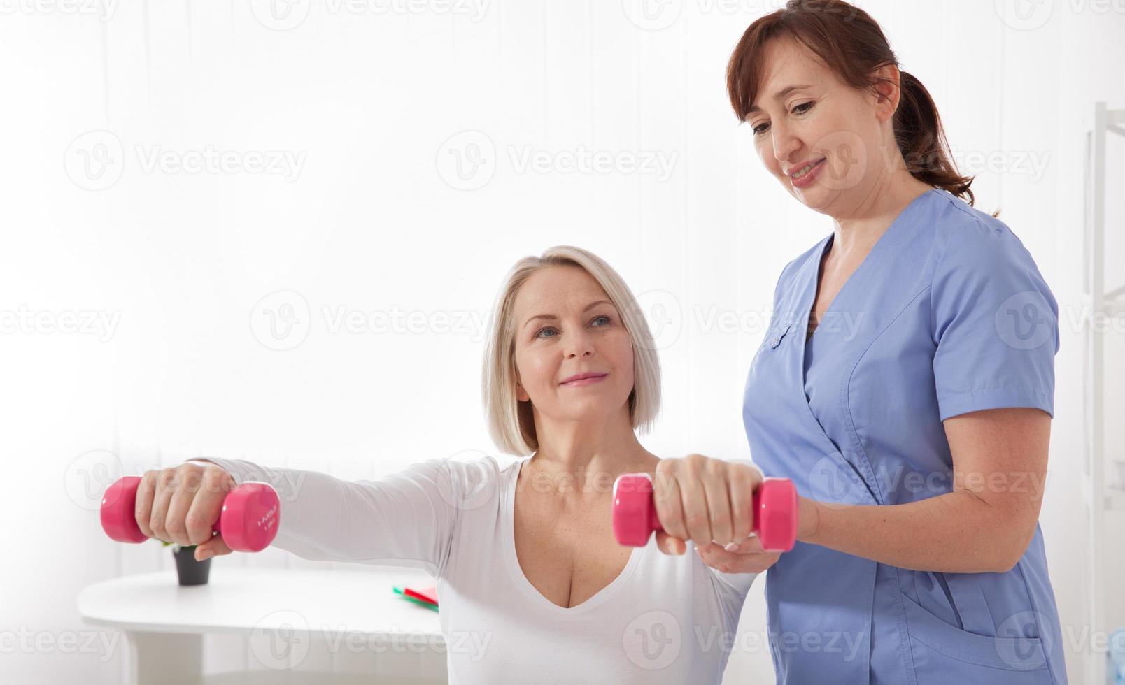 A physiotherapist helps an older woman recover from an injury through exercise with dumbbells. photo