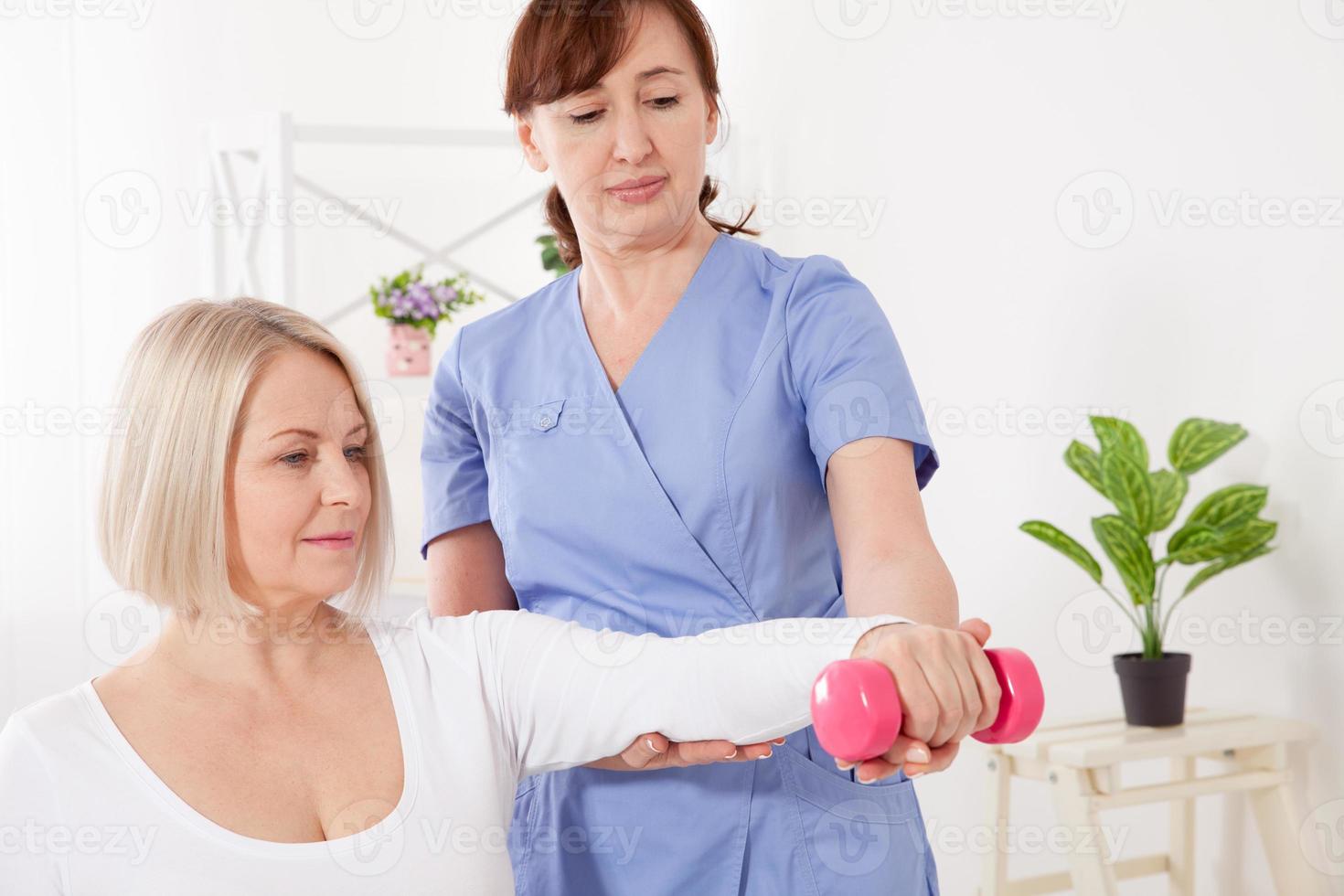 A physiotherapist helps an older woman recover from an injury through exercise with dumbbells. photo