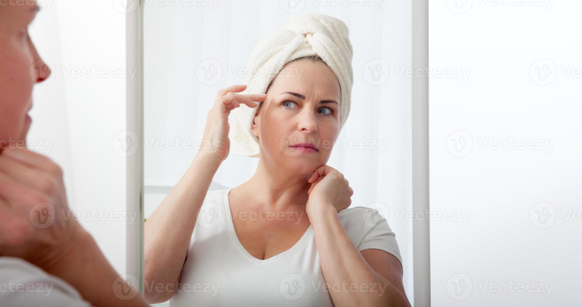 Forty years old woman looking at wrinkles in mirror. Plastic surgery and collagen injections. Makeup. Macro face. Selective focus on the face. photo