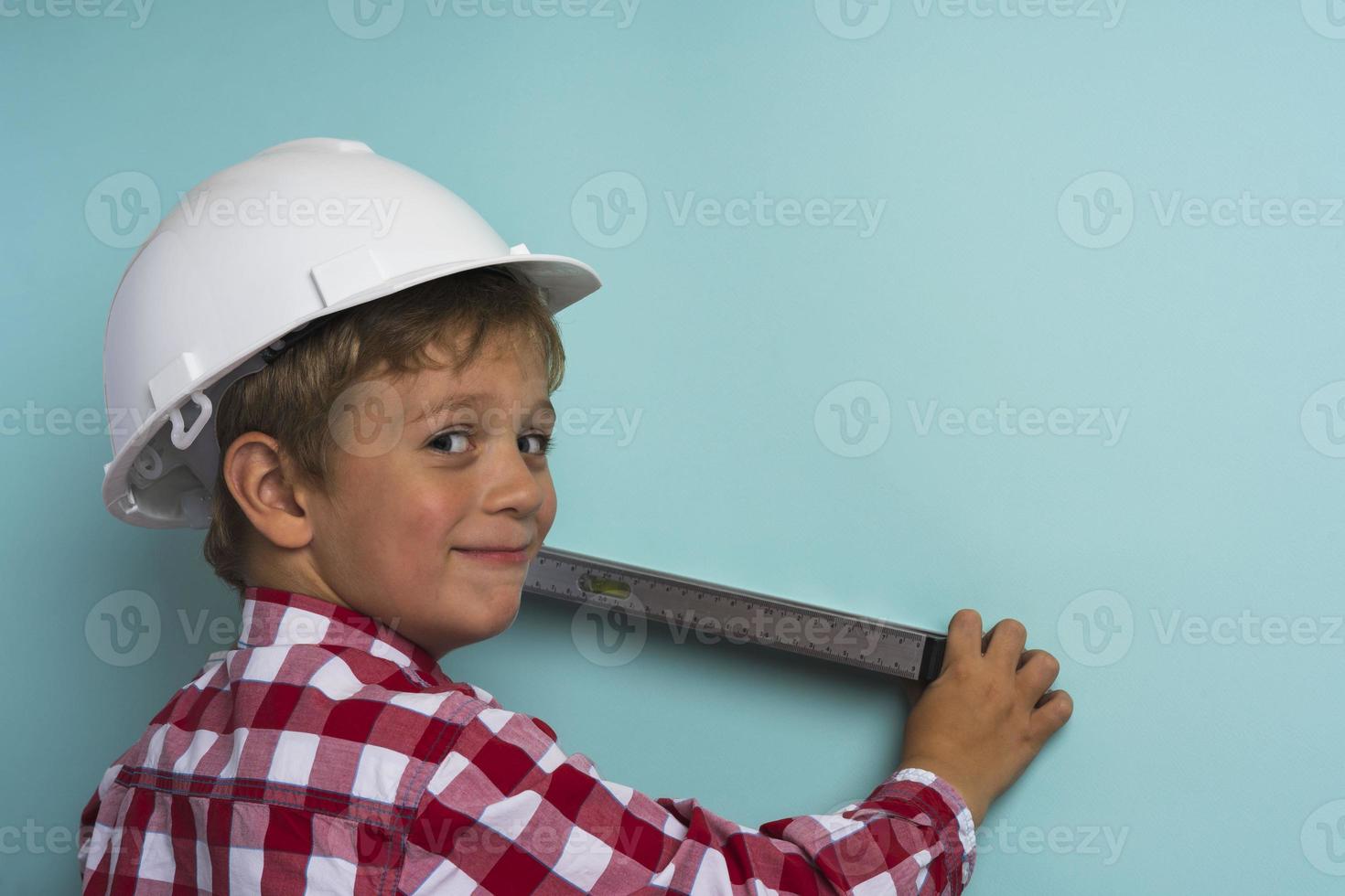 un chico lindo con una camisa a cuadros sostiene un nivel de construcción en sus manos, un retrato de un pequeño constructor foto