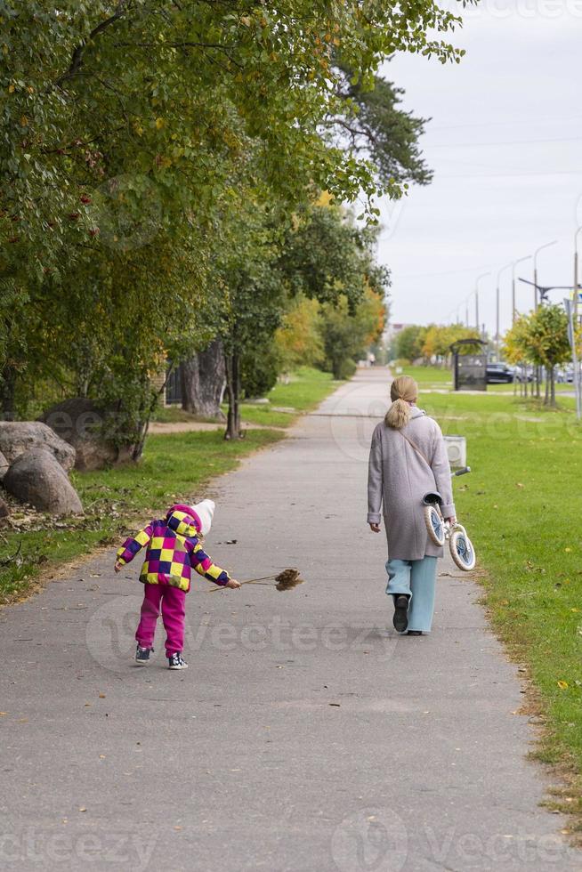 una madre joven con un niño pequeño caminando por los senderos del parque en otoño, una bicicleta para niños, una bicicleta foto