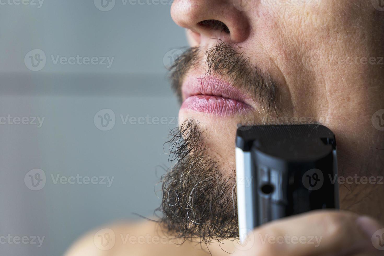 a man cuts his beard and mustache with an electric razor, time to shave, beard and mustache care photo